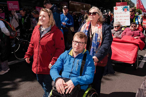 Eine Frau schiebt einen jungen Mann im Rollstuhl. Daneben eine weitere junge Frau. 