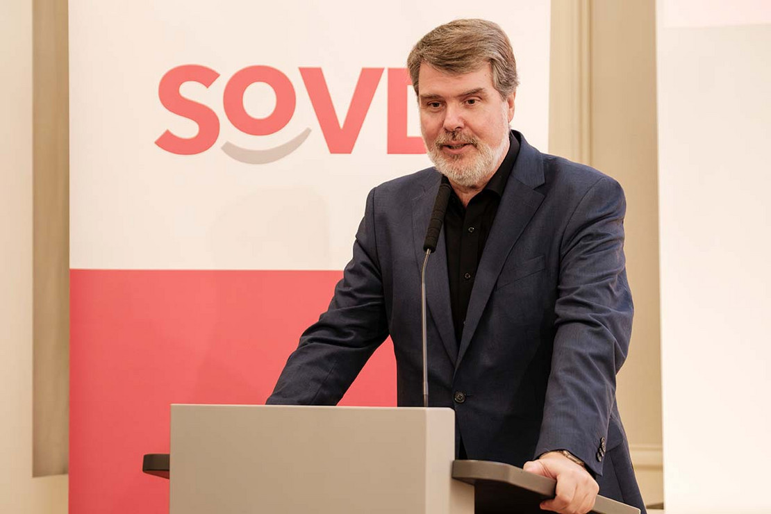 Mann steht an einem Rednerpult vor einem SoVD-Logo. 