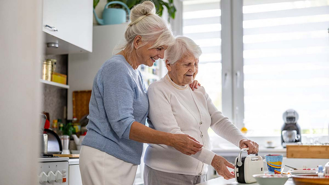 Eine ältere ist mit ihrer Mutter in der Küche und hält sie fest. 