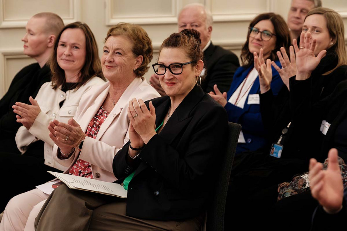 Drei Frauen sitzen auf Stühlen und applaudieren. 