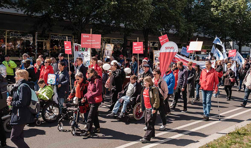 Mehrere Menschen in roter Kleidung mit Schildern und SoVD-Fahnen. 