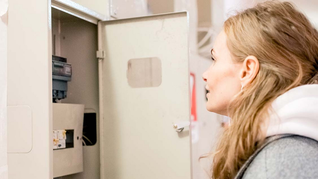 Junge Frau blickt in den Sicherungskasten in ihrer Wohnung. 