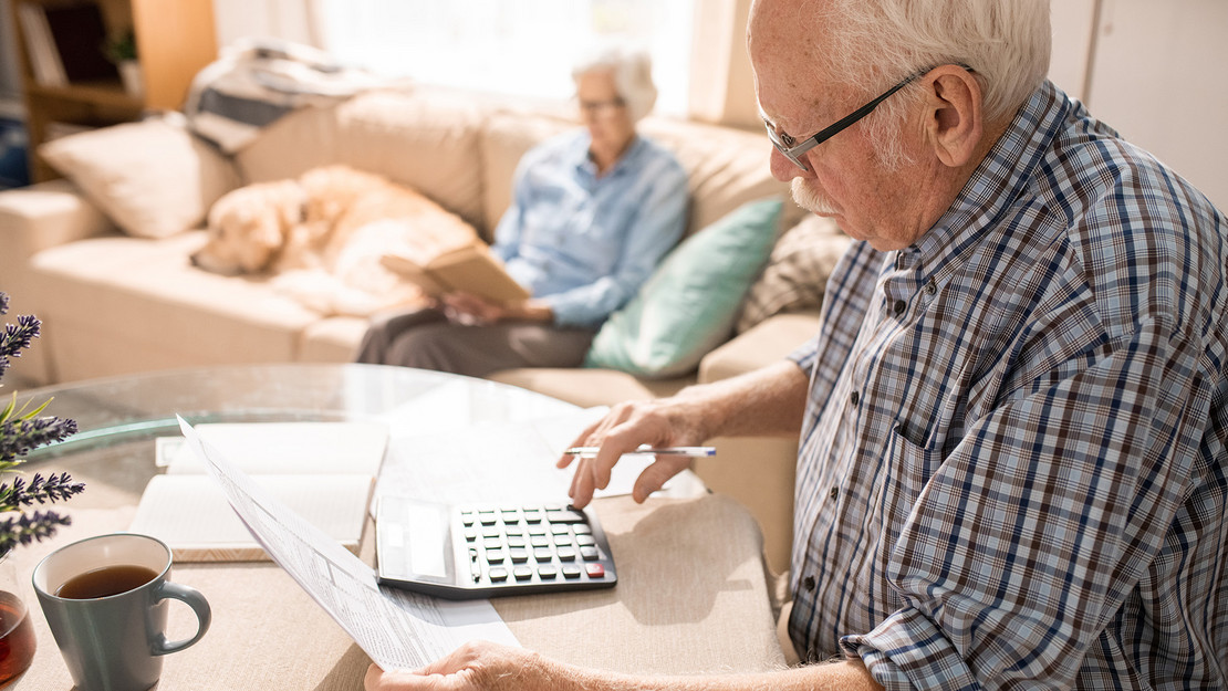 Alter Mann mit sitzt mit Taschenrechner am Tisch