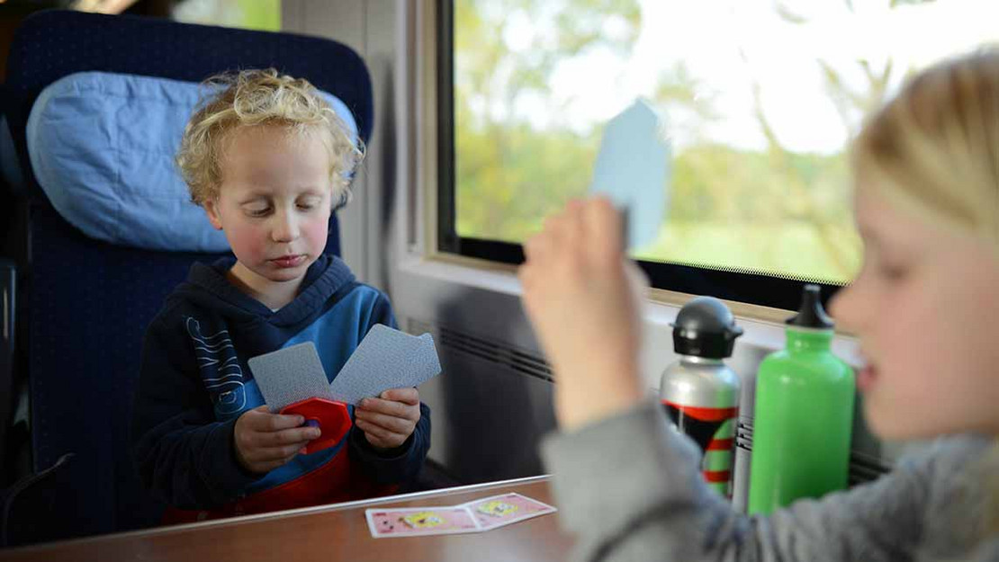 Zwei junge Kinder spielen in einem Zug am Tisch Karten. 