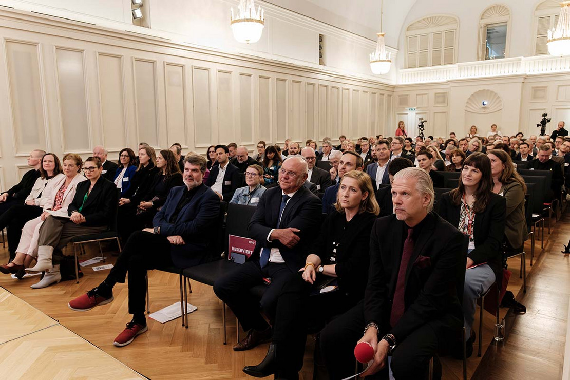 Ein Saal mit vielen Stühlen, auf denen Menschen sitzen. 