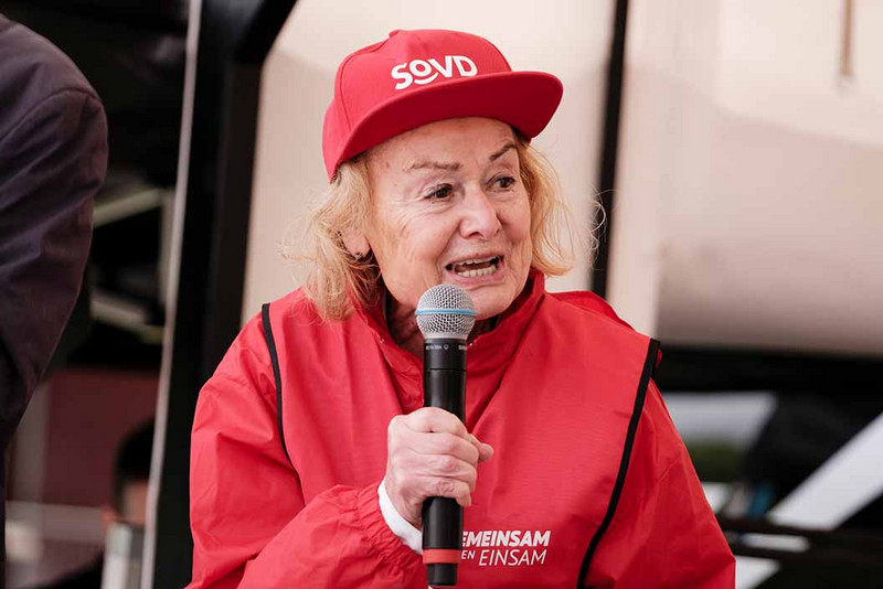 Frau mit SoVD-Mütze und Mikrofon in der Hand.