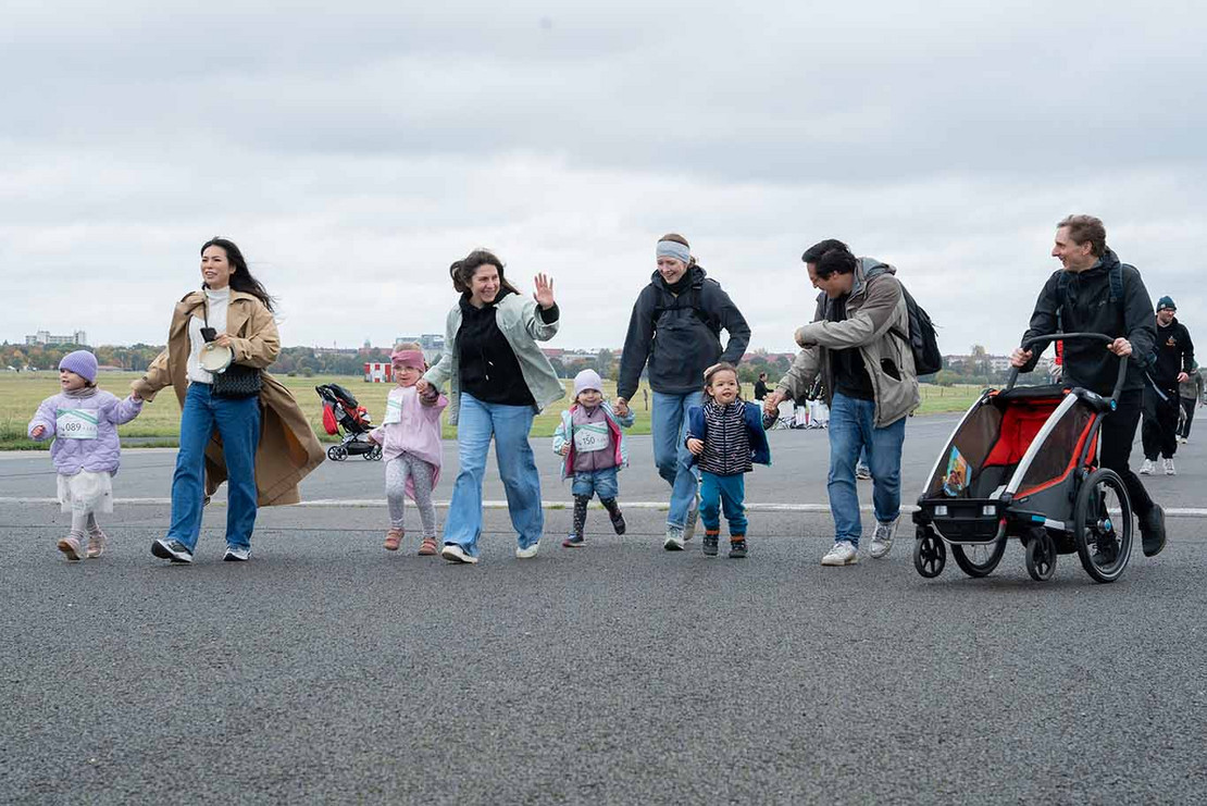 Vier Kinder und vier Erwachsene laufen auf die Kamera zu. 