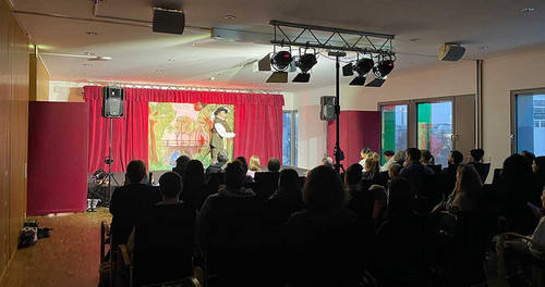 Mann steht auf einer Bühne in einem vollbesetzten Raum.