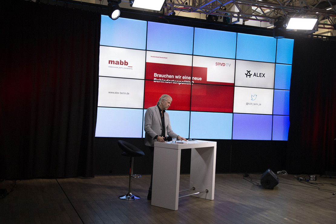 SoVD-Pressesprecher vor einer Displaywand.