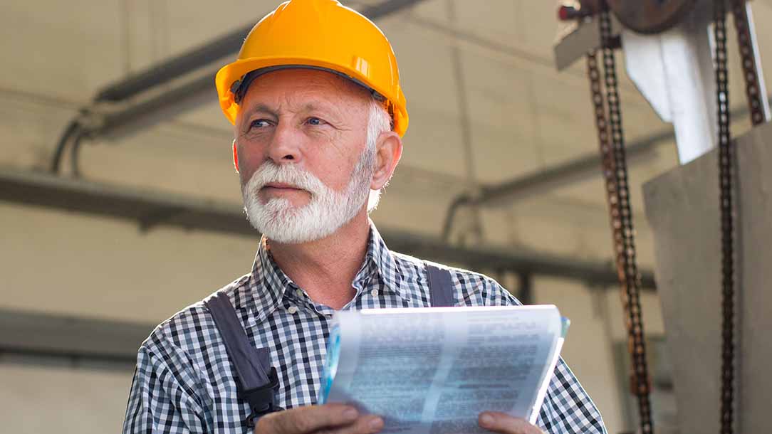 Älterer Arbeit mit einem Klemmbrett steht in einer Fabrik.
