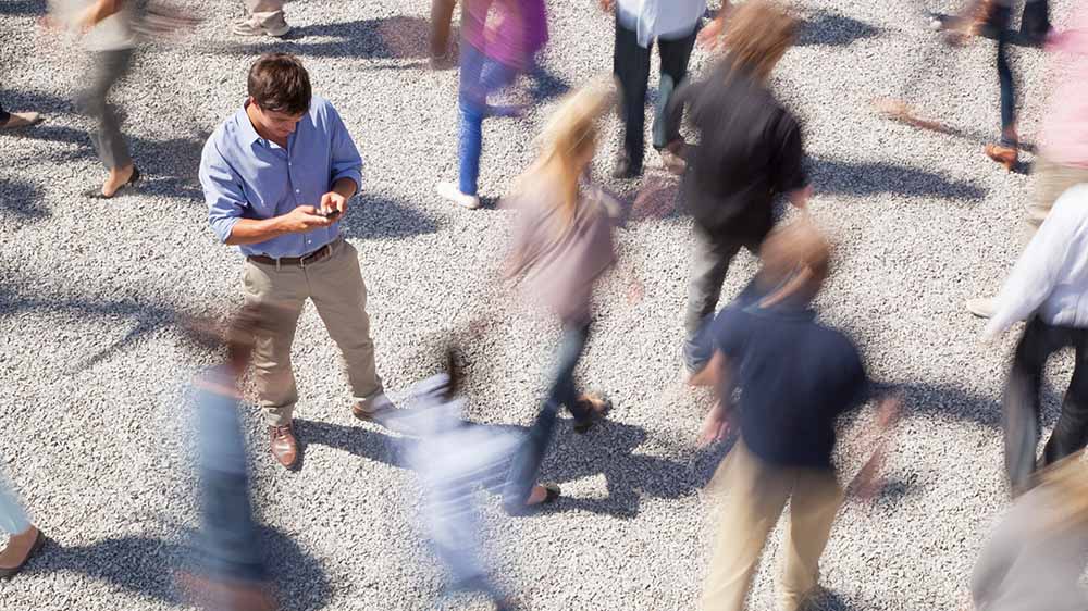 Mann in einer Menschenmenge blickt auf sein Handy