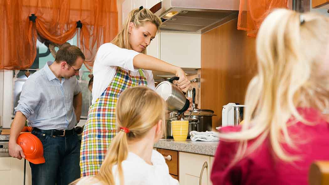 Frau und Kinder in der Küche, während Mann gerade nach Hause kommt.