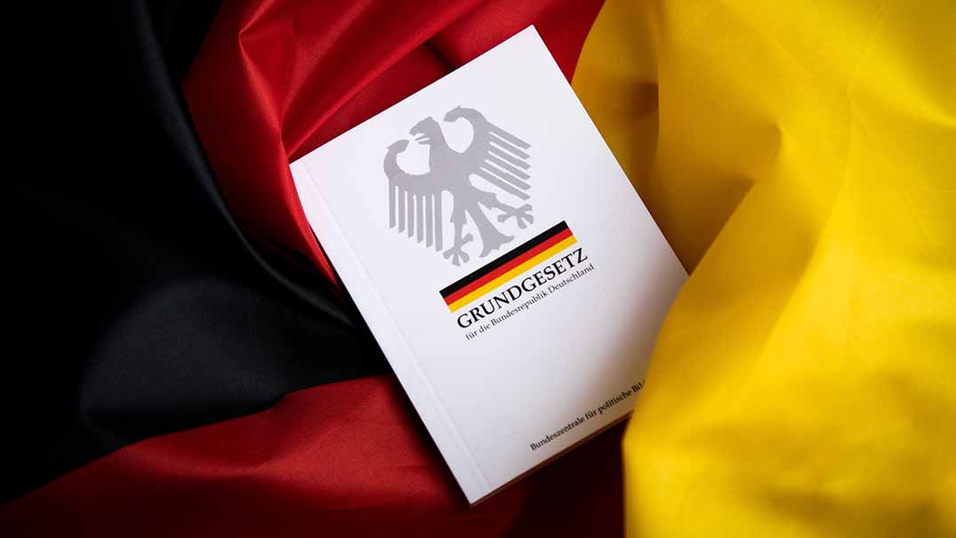 Das Grundgesetz als Buch vor einem schwarz-rot-goldenen Hintergrund.